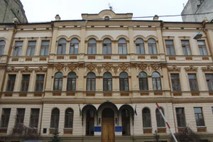 Орнементований бежевий фасад будівлі з прапорами України та ЄС біля входу